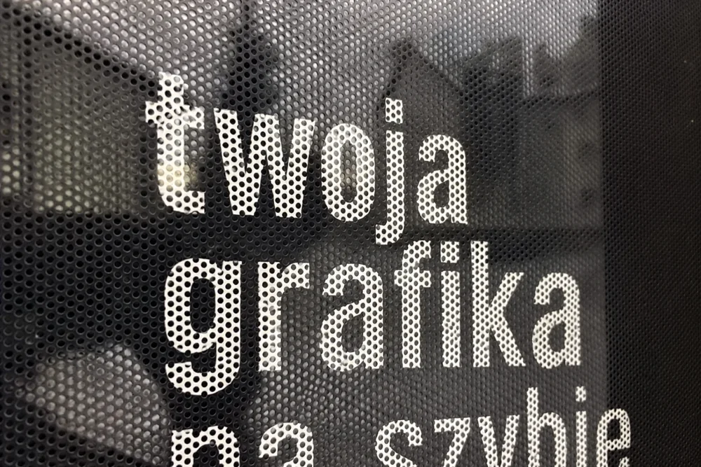 Folia OWV One Way Vision z własnym nadrukiem Folia OWV z białym napisem na ciemnej perforowanej folii – zbliżenie na perforację (wizualizacja)
